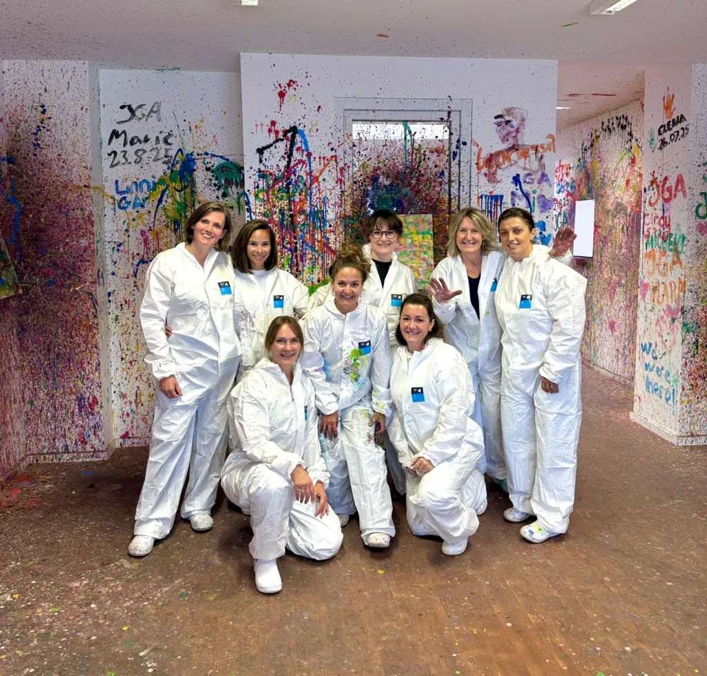 Eine Gruppe Frauen in weißen Overalls vor bunt bespritzten Wänden