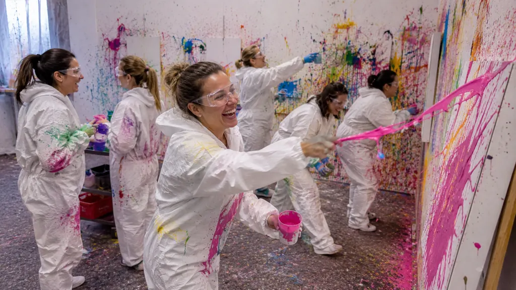 Eine Frau im weißen Overall schleudert pinke Farbe auf eine Leinwand