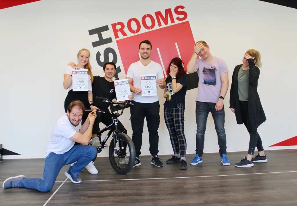 Freunde posieren lachend mit Urkunden, einer kniet vor einem BMX-Rad