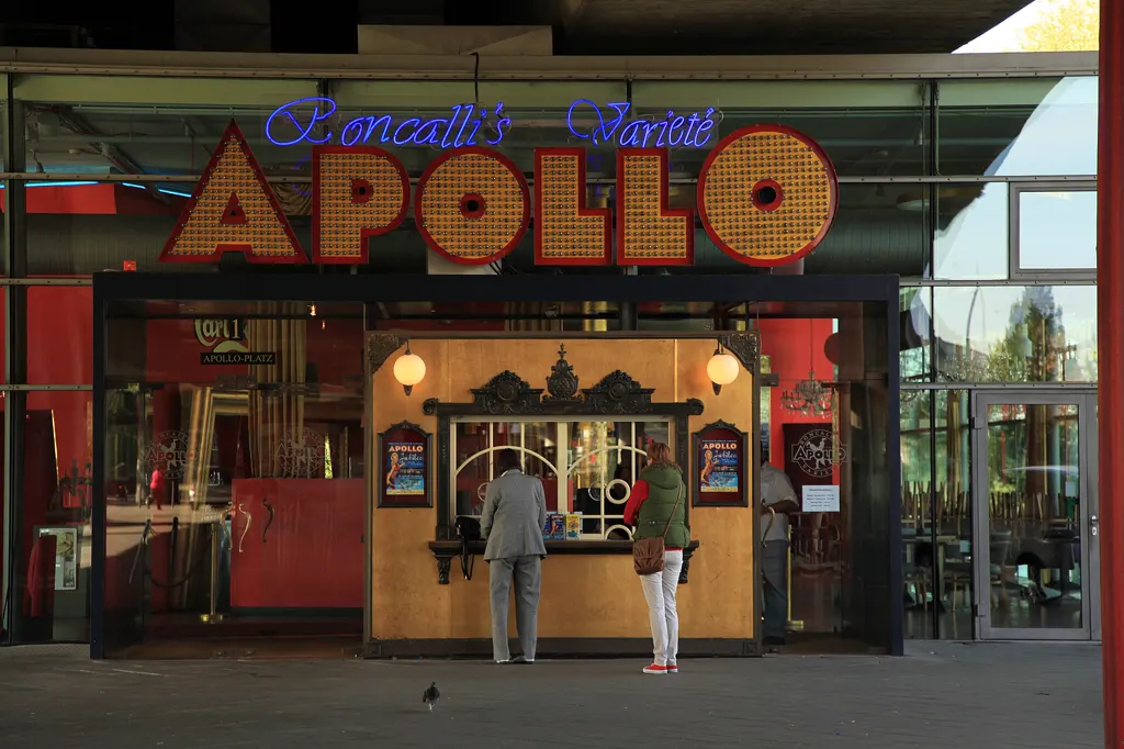 Eingang des Apollo Varieté unter der Rheinkniebrücke: Kassenhäuschen mit großer APOLLO-Leuchtschrift, zwei Gäste von hinten