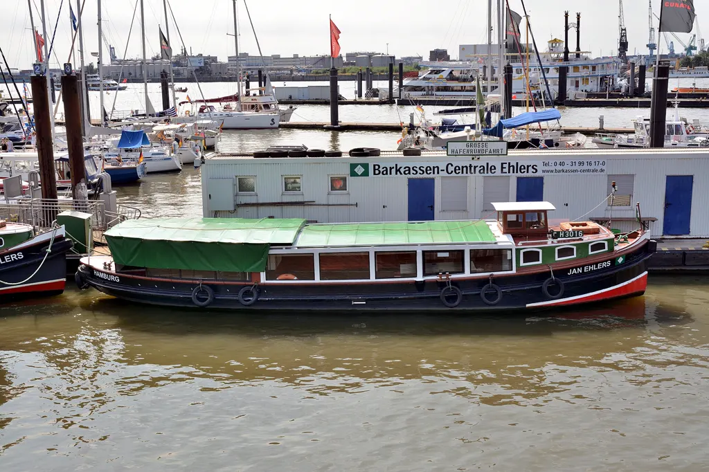 Die Traditionsbarkasse „Jan Ehlers“ mit grünem Sonnendach liegt vor dem Ponton der Barkassen-Centrale Ehlers mit dem Schild „Große Hafenrundfahrt“.