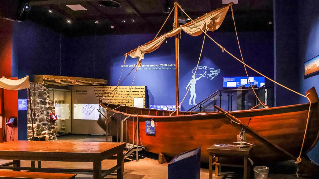 Nachgebautes Fischerboot mit Segel im Ausstellungsraum „Leben am See Gennesaret vor 2000 Jahren“, davor ein Holztisch, dunkelblaue Wand