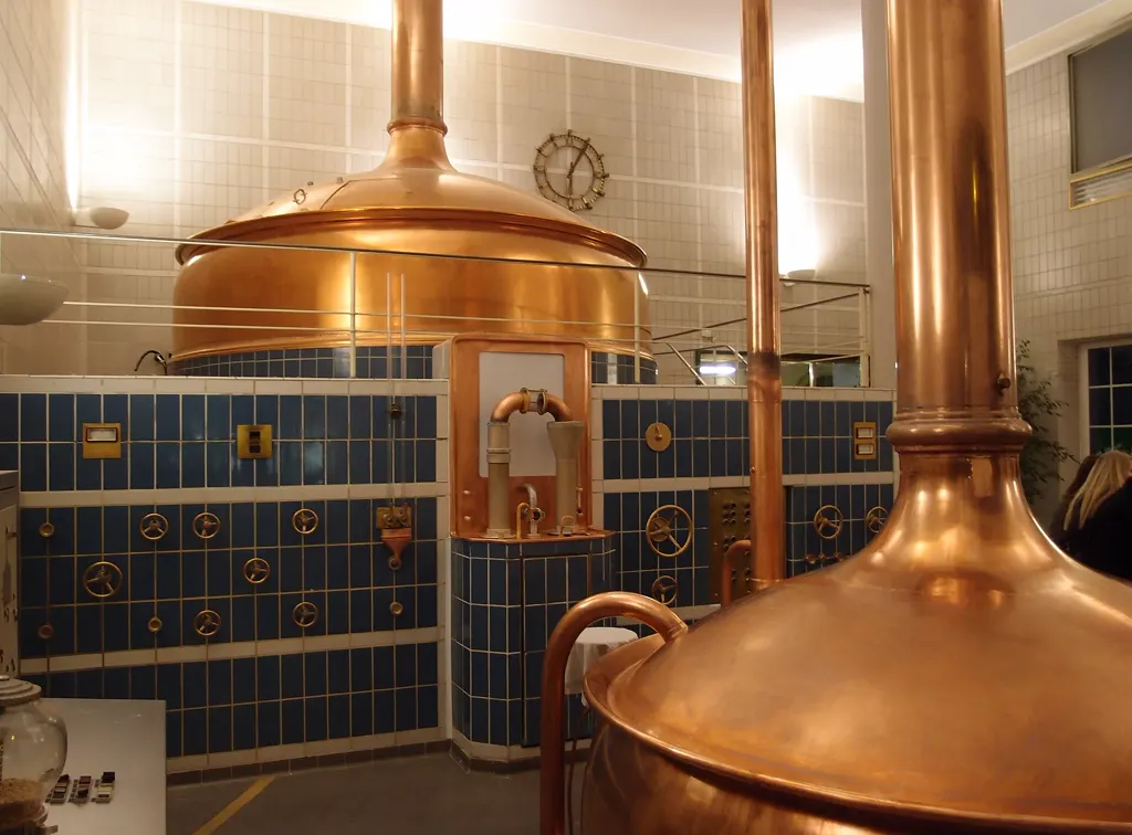 Historisches Sudhaus der Brauerei in Köln-Kalk mit blank polierten Kupferkesseln vor blau gefliesten Wänden mit Messingrädern.