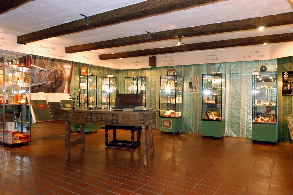 Ausstellungsraum des Duftmuseums mit Vitrinen voller historischer Flakons, Holzbalkendecke und Epochen-Schriftbändern