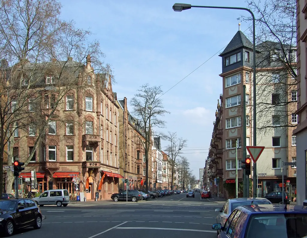 Blick von der Schweizer Straße in die Textorstraße in Sachsenhausen mit Gründerzeithäusern, roten Restaurant-Markisen und blauem Himmel.