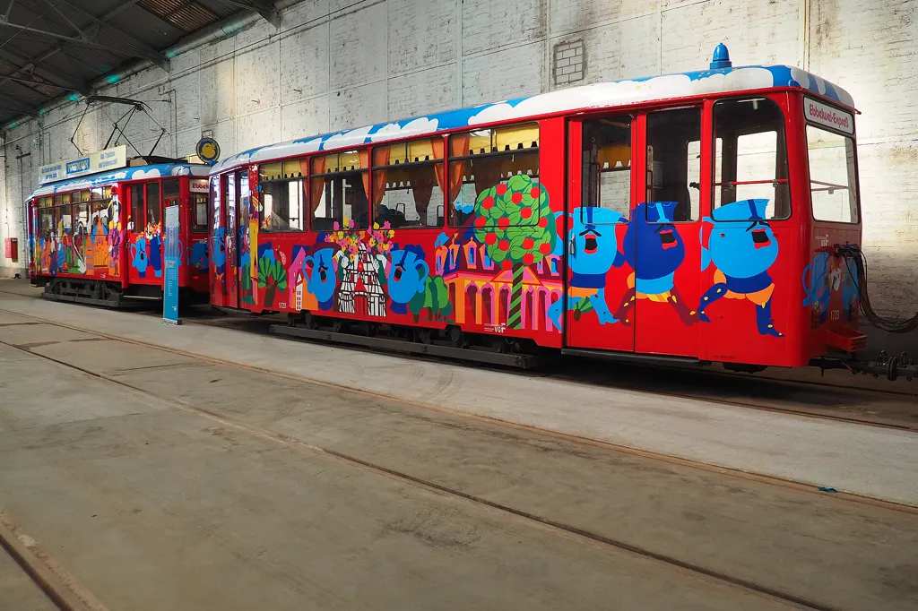Seitenansicht der beiden rot bemalten Wagen des Ebbelwei-Expreß mit blauen Bembel-Figuren, Apfelbaum und Frankfurter Häusern auf der Wagenwand, abgestellt in einer hellen Halle des Betriebshofs Gutleut.