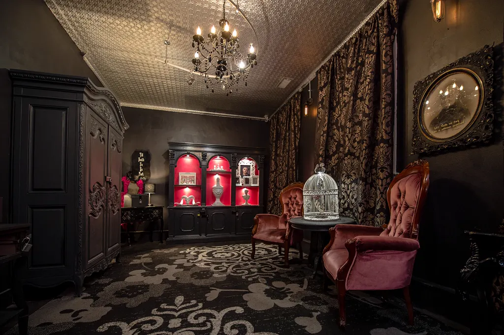 Escape-Room im viktorianischen Stil: Kronleuchter, verschlossener Schrank, beleuchtete Vitrine, Samtsessel und Vogelkäfig; ohne Personen