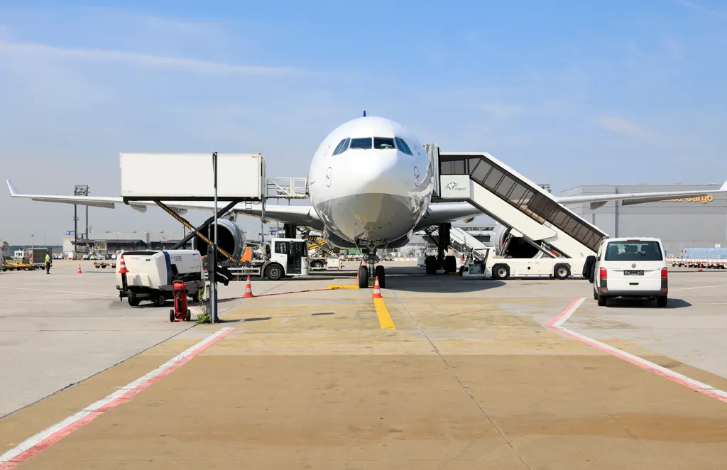 Flugzeug in Parkposition auf dem Vorfeld, frontal, mit Passagiertreppe, Catering-Hubwagen und Abfertigungsfahrzeugen, blauer Himmel