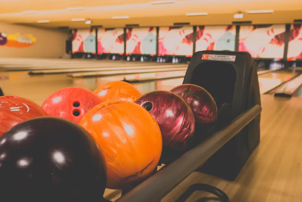 Bunte Bowlingkugeln im Kugelrücklauf vor den unscharfen Bahnen einer hellen Bowlinghalle.