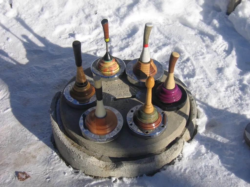 Sechs Eisstöcke mit hölzernen Stielen auf einem Betonring im Schnee.