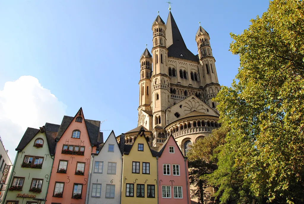 Bunte schmale Giebelhäuser am Fischmarkt in der Kölner Altstadt, dahinter der Turm der romanischen Kirche Groß St. Martin vor blauem Himmel.