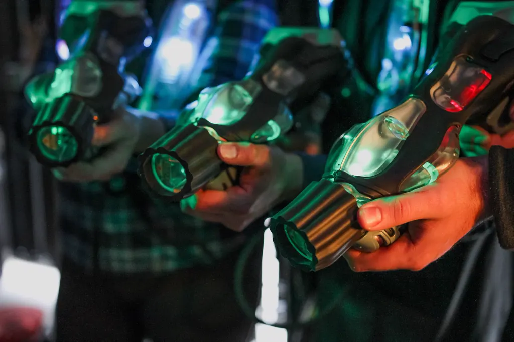 Nahaufnahme mehrerer Hände, die im Halbdunkel grün leuchtende Lasertag-Phaser halten.