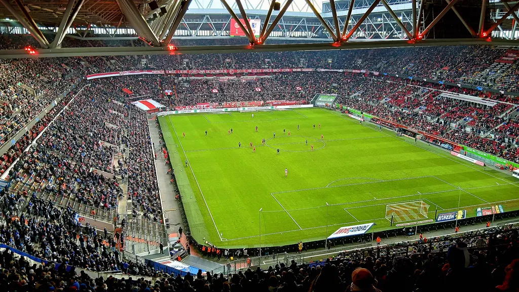 Blick vom Oberrang in die voll besetzte Merkur Spiel-Arena mit Stahldach und grünem Spielfeld.