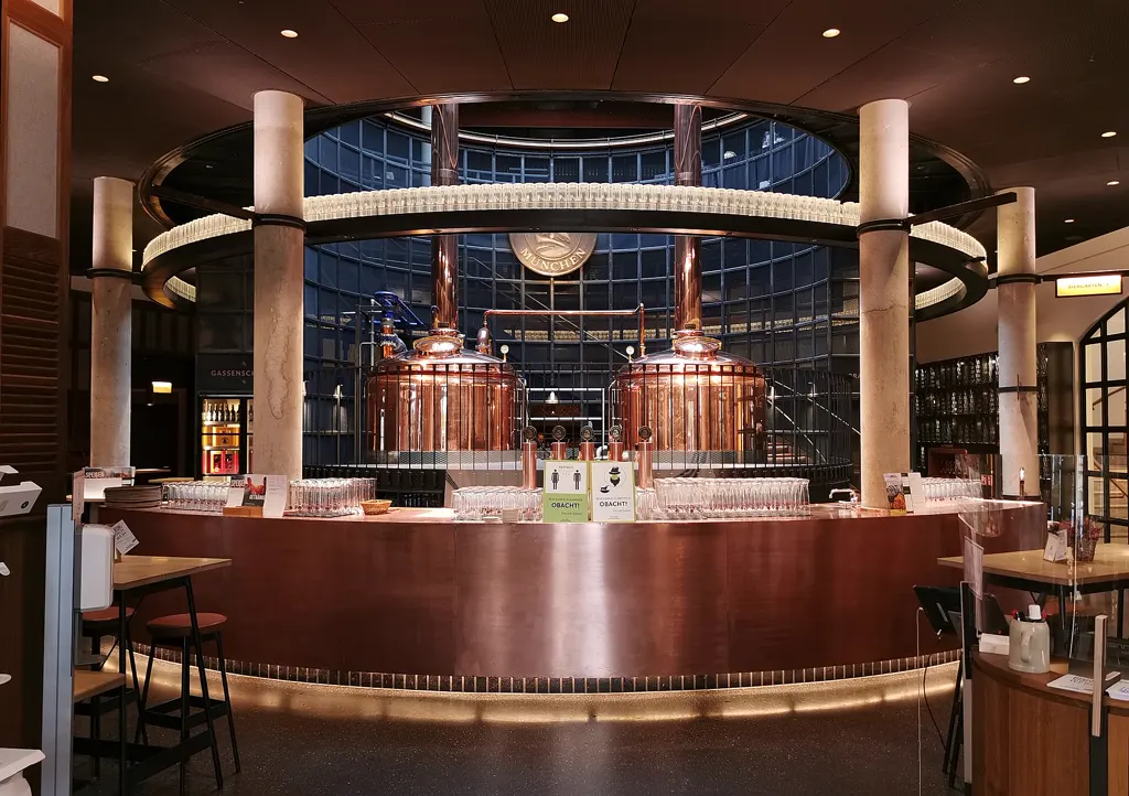 Rotunde im Wirtshaus Paulaner am Nockherberg: zwei kupferne Sudkessel der Hausbrauerei hinter dem runden Tresen, Gläser auf der Theke; ohne Personen