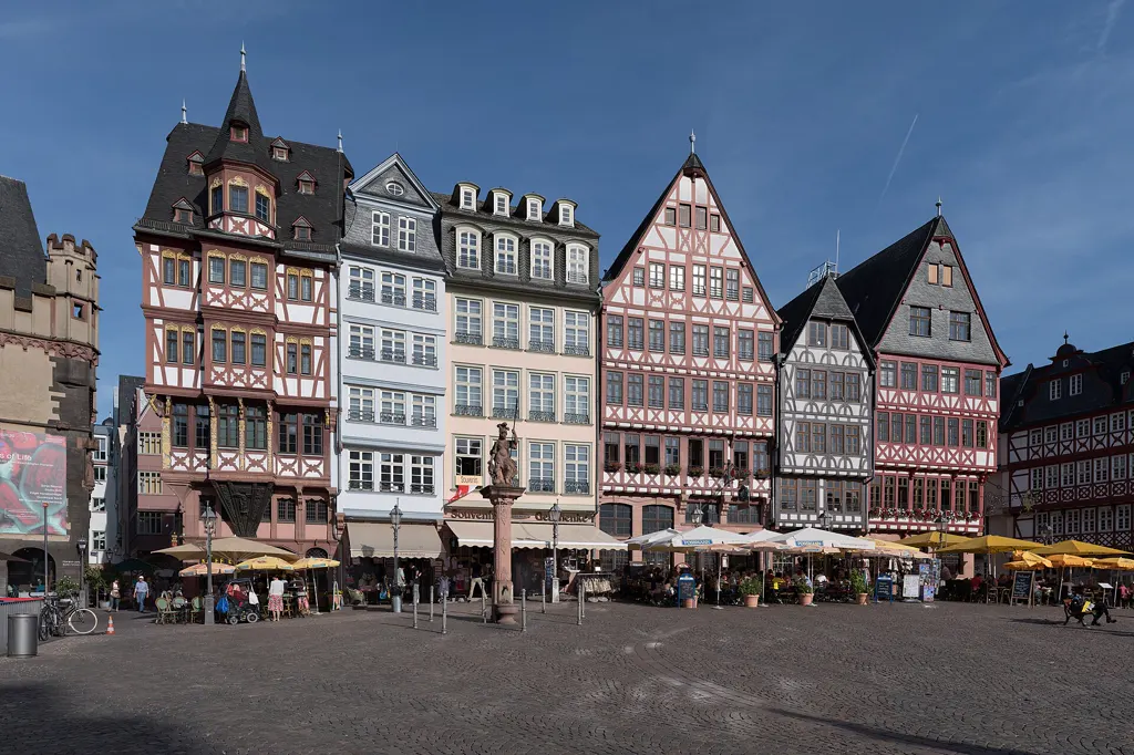 Die Fachwerkhäuser der Ostzeile am Römerberg (Samstagsberg) in der Frankfurter Altstadt bei Sonne und blauem Himmel, davor Café-Schirme und wenige Passanten.