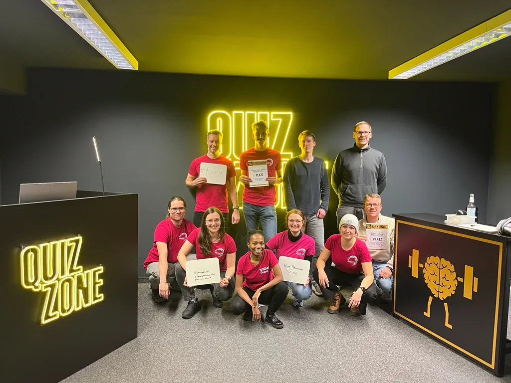 Ein Team mit Urkunden und Schildern vor einer gelben Leuchtschrift